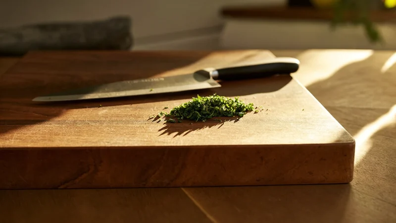 Dickes Nussbaum-Hirnholzbrett mit schlichtem Kochmesser und gehackten Kräutern