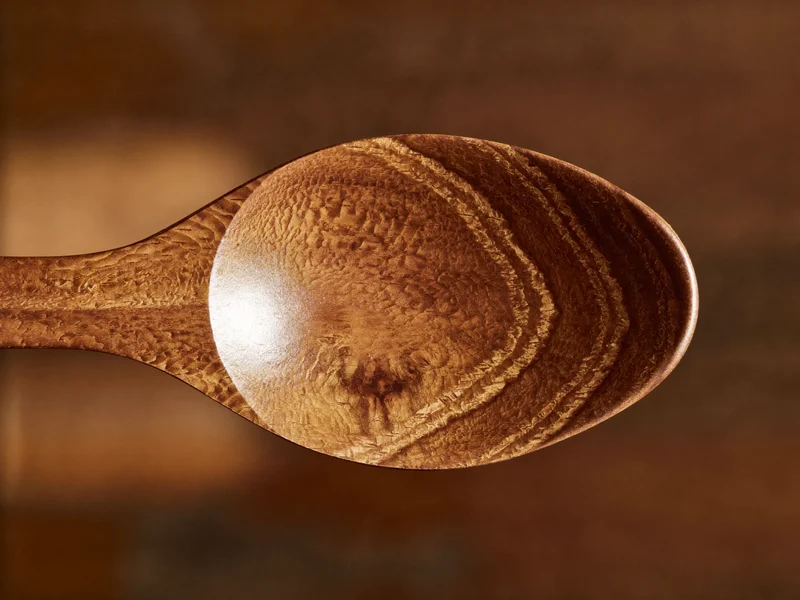 Nahaufnahme der Holzmaserung eines frisch geölten Löffels mit Öltropfen